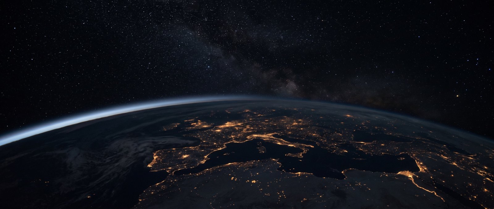 Earth at night seen from orbit, city lights scattered across the dark landmass